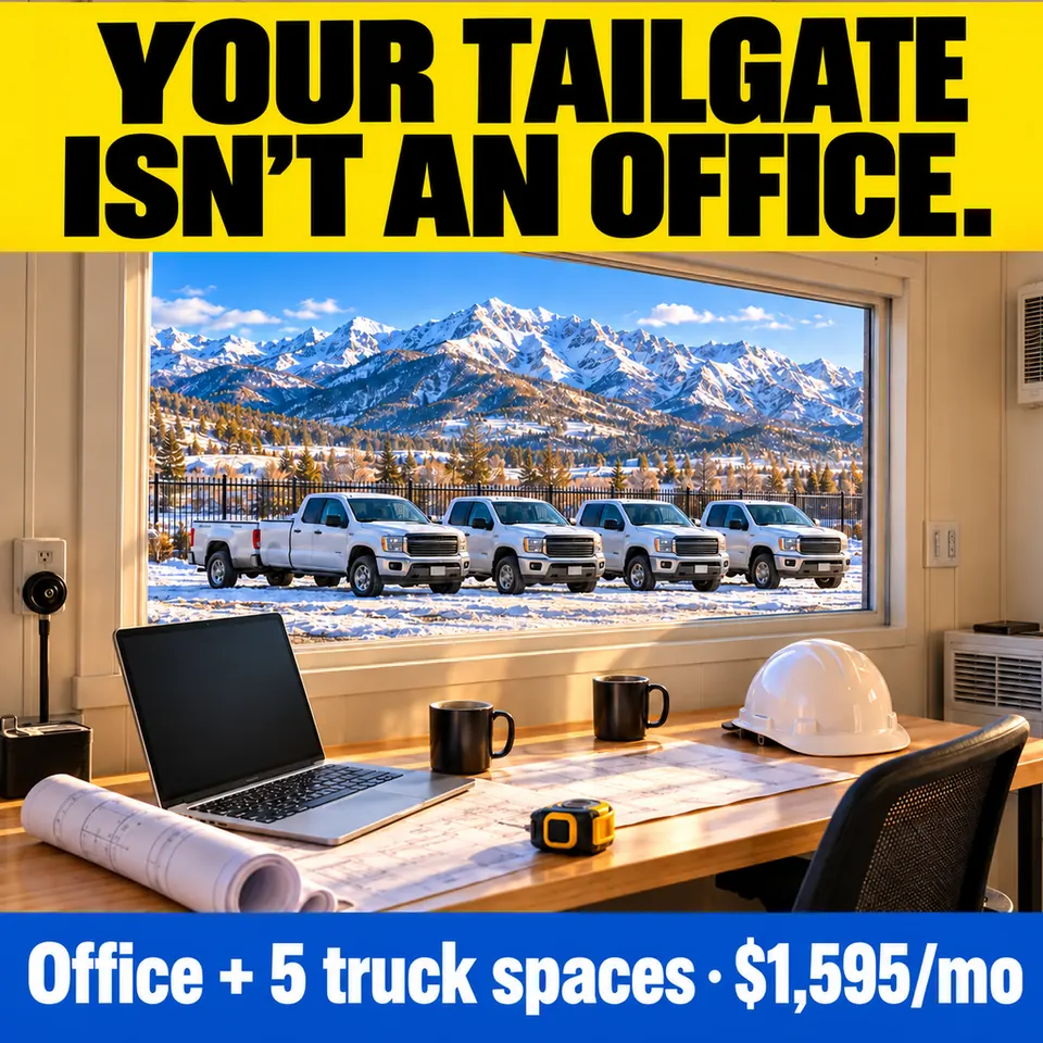 Inside a private office: laptop, coffee mug, rolled plans and a white hard hat on a desk, five white pickups parked outside the window under snowy mountains. Text: Your tailgate isn't an office. Office + 5 truck spaces, $1,595/mo.